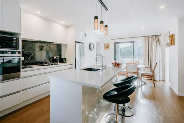 A bright, well-maintained vacation rental kitchen featuring a white island with black bar stools, built-in appliances, pendant lighting, and an open dining space — illustrating the standard guests expect after a thorough turnover clean.