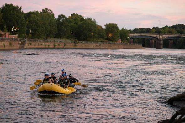 Group rafting on the Chattahoochee River in Columbus, Georgia, with a scenic riverside backdrop and a historic bridge in the distance.
