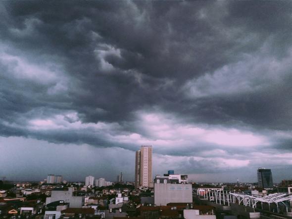 A wide-angle view of a city skyline engulfed under heavy, dark grey storm clouds. In the context of Vrbo cancellation policies, this represents severe weather events and natural disasters. These qualifying, large-scale disruptions activate Vrbo's Extenuating Circumstances Policy, which overrides a host's standard cancellation policy to protect both parties when travel is impossible.